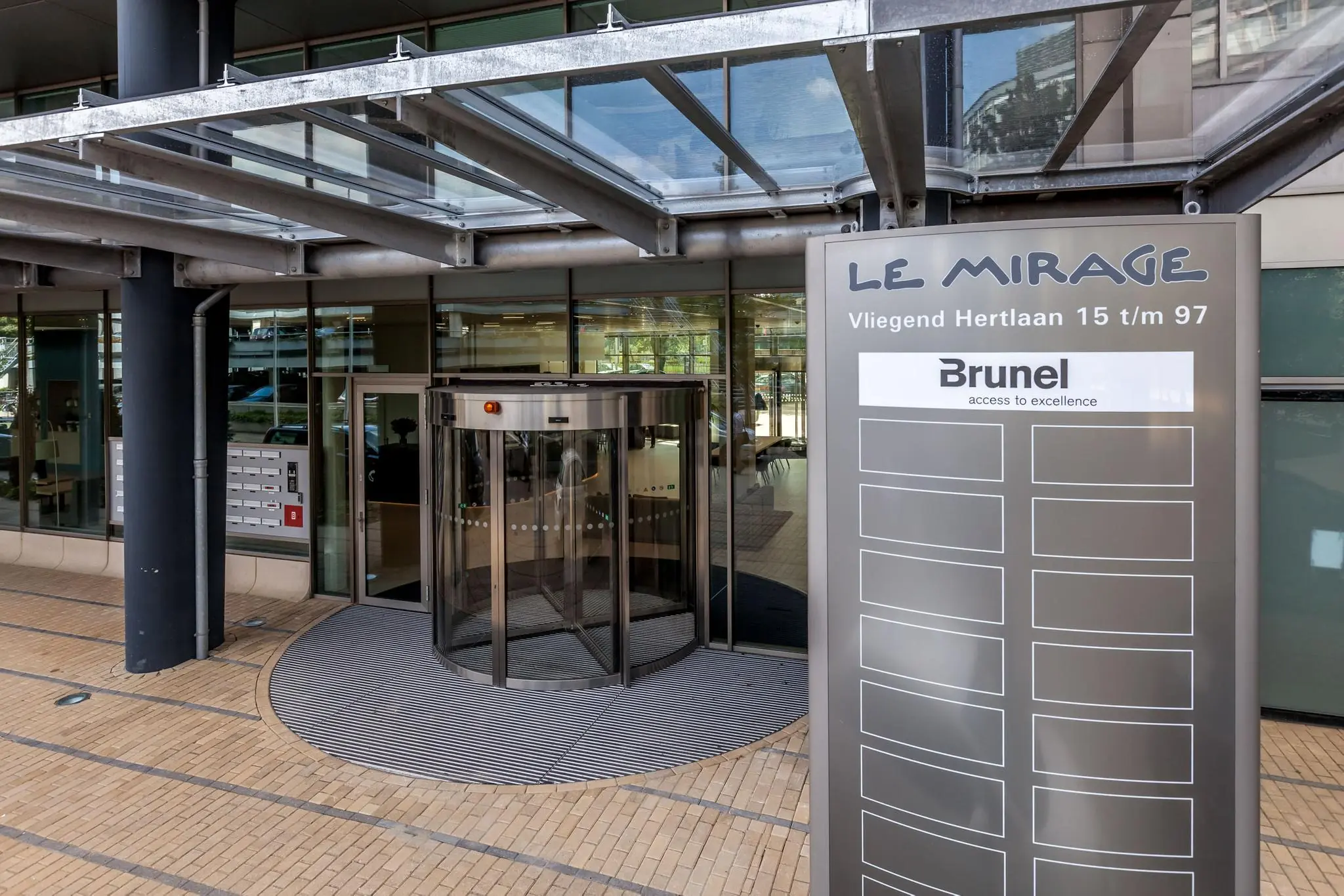 Ingang van kantoorgebouw Le Mirage aan de Vliegend Hertlaan met een draaideur en een bedrijvenbord waarop Brunel vermeld staat.